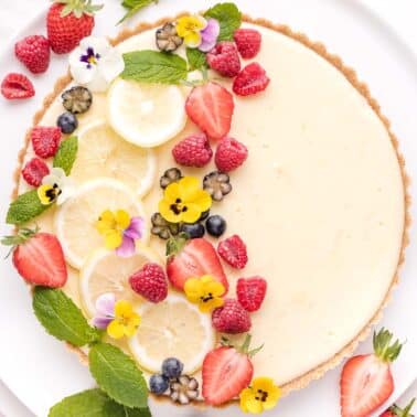 lemon icebox pie garnished with fresh berries, lemon slices, and edible flowers on a white plate.
