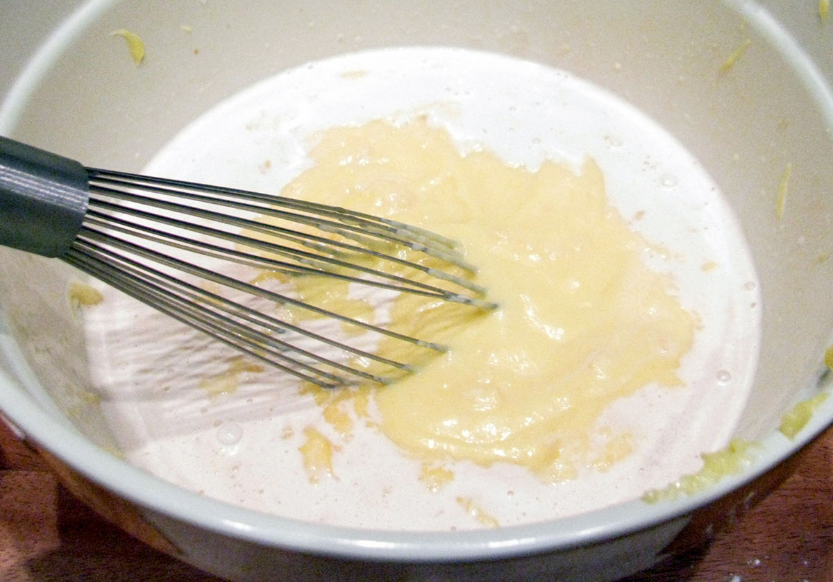 A metal whisk in a bowl with remnants of a pale yellow eggs, suggesting a recently mixed ingredient for baking or cooking.