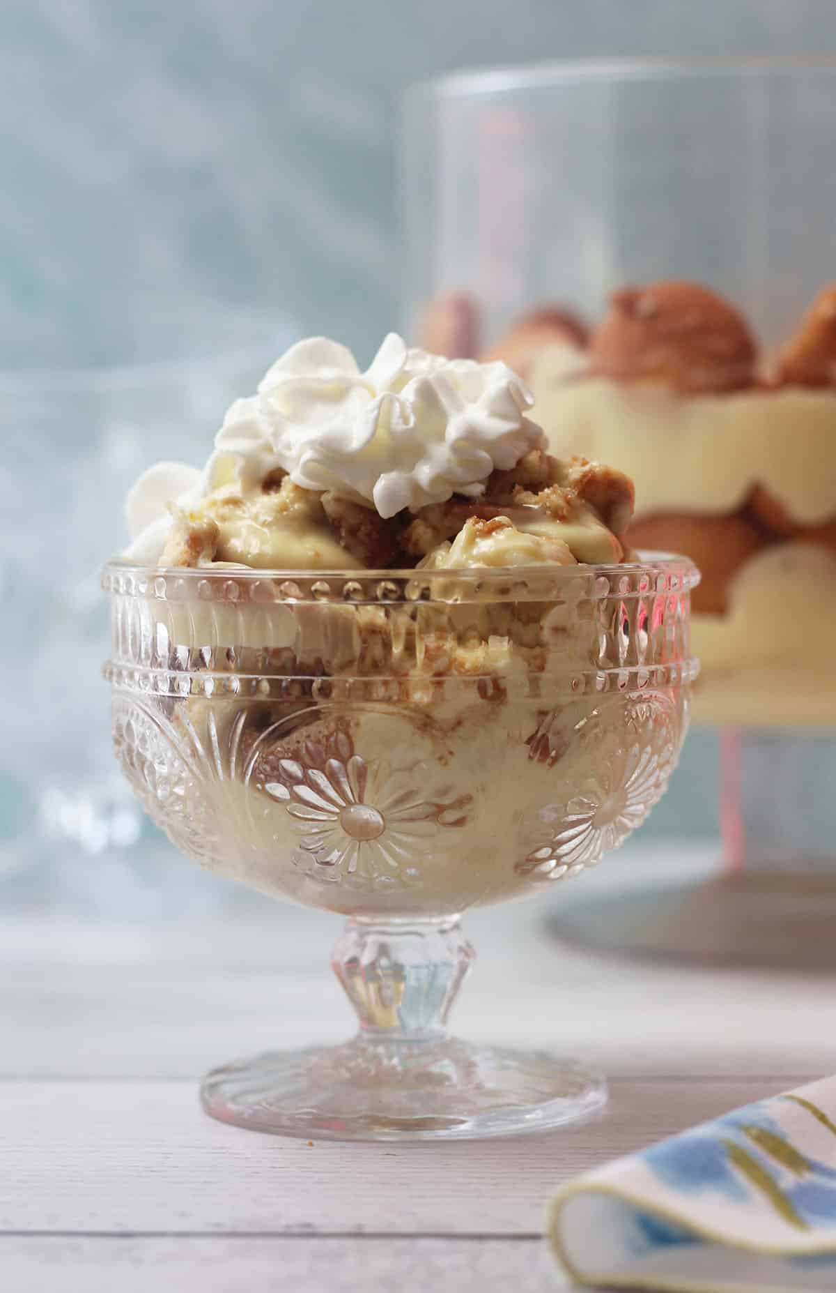 A glass bowl of banana pudding topped with whipped cream and cookie crumbles placed on a wooden table.