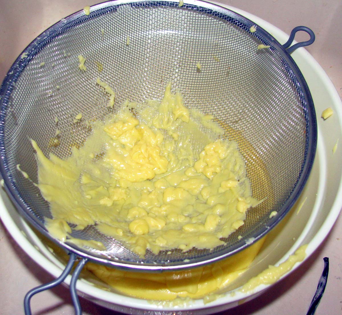 Custard strained in a metal sieve over a white bowl.