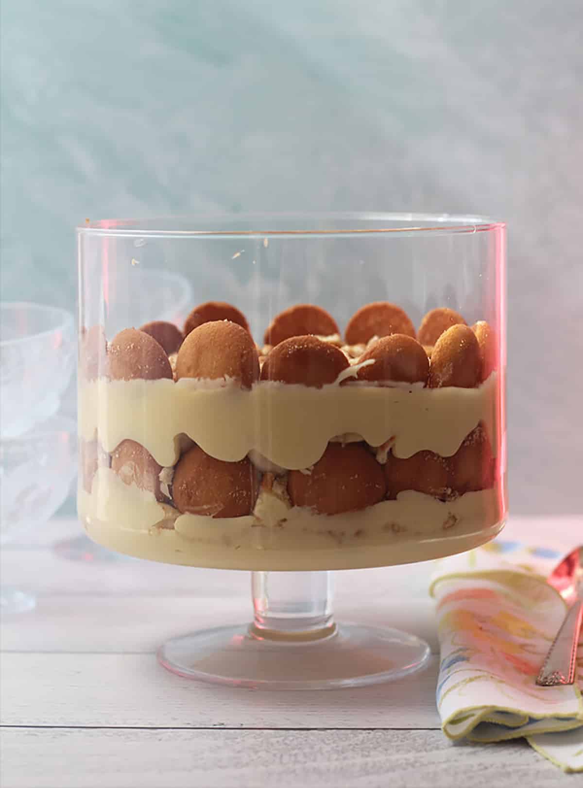 A trifle dessert with layers of custard, bananas, and vanilla wafers in a glass bowl.