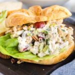 Croissant sandwich with lettuce on a croissant, served on a wooden board with a blurred background.