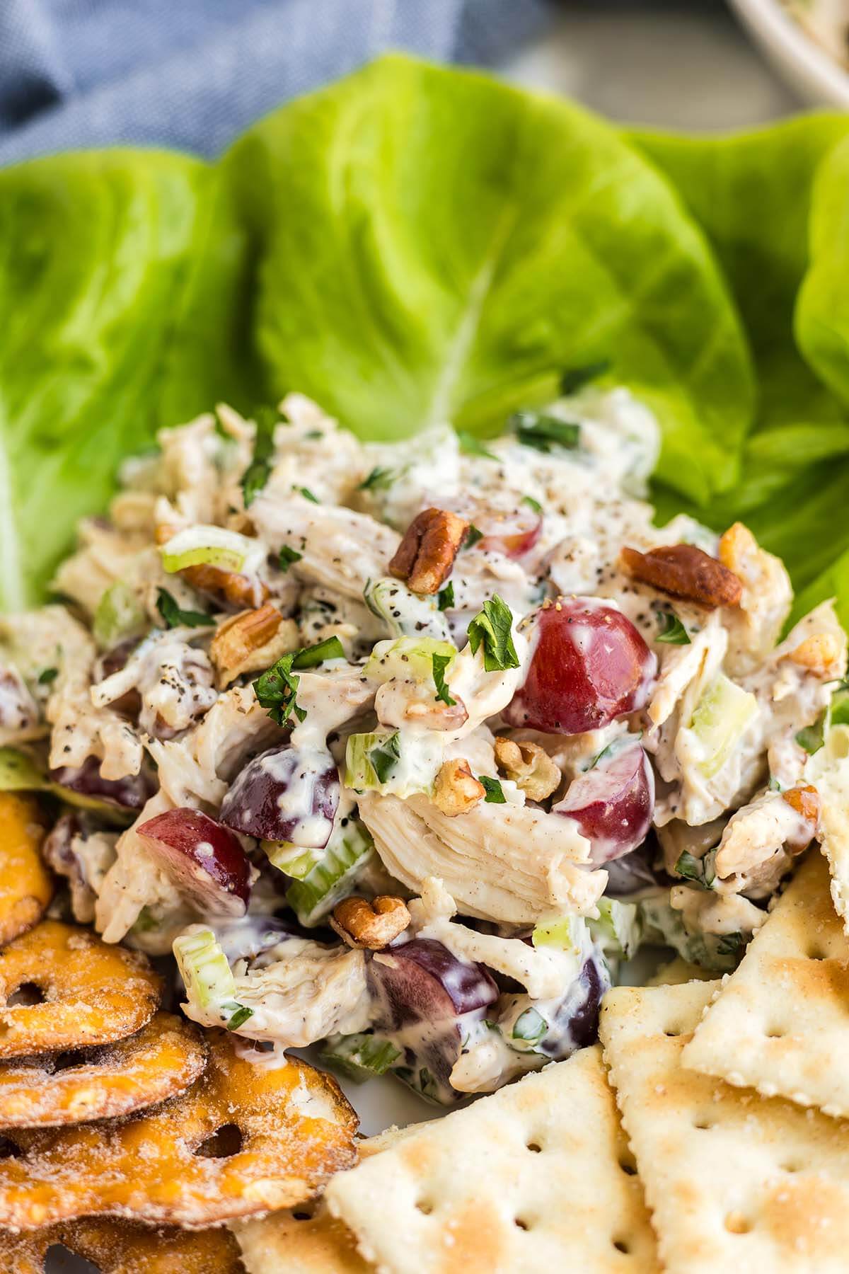 Chicken salad with grapes, pecans, and herbs served in a lettuce wrap, accompanied by golden-brown crackers.