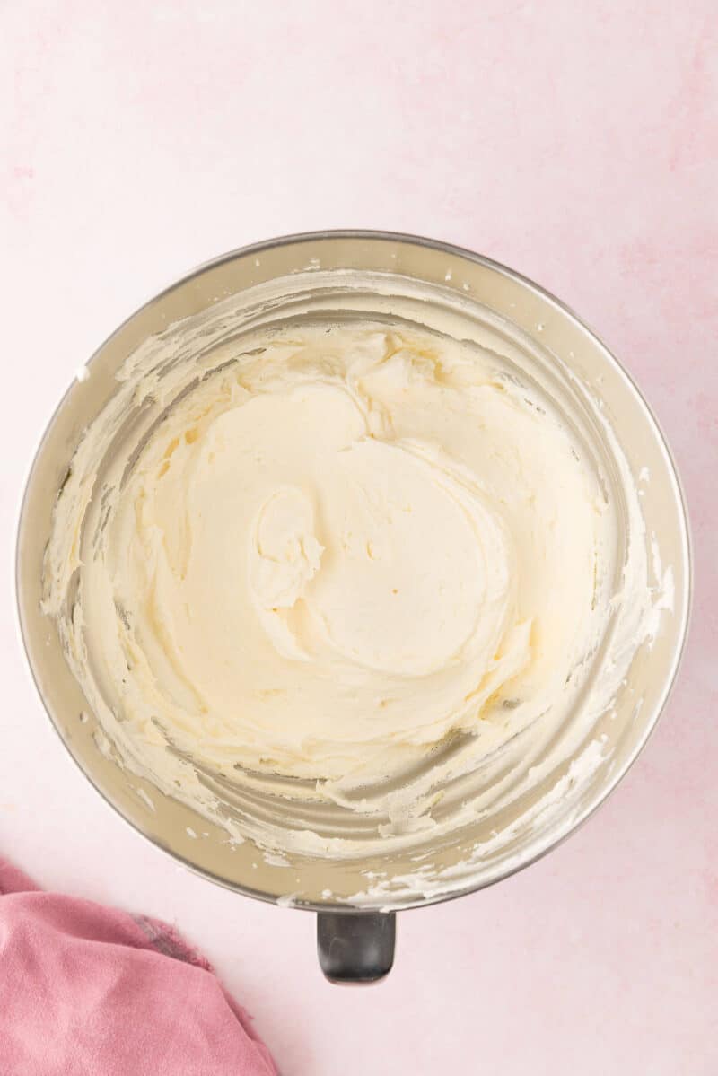 Top view of a metal mixing bowl on a pink surface with cake batter or dough mixed inside, next to a pink cloth.