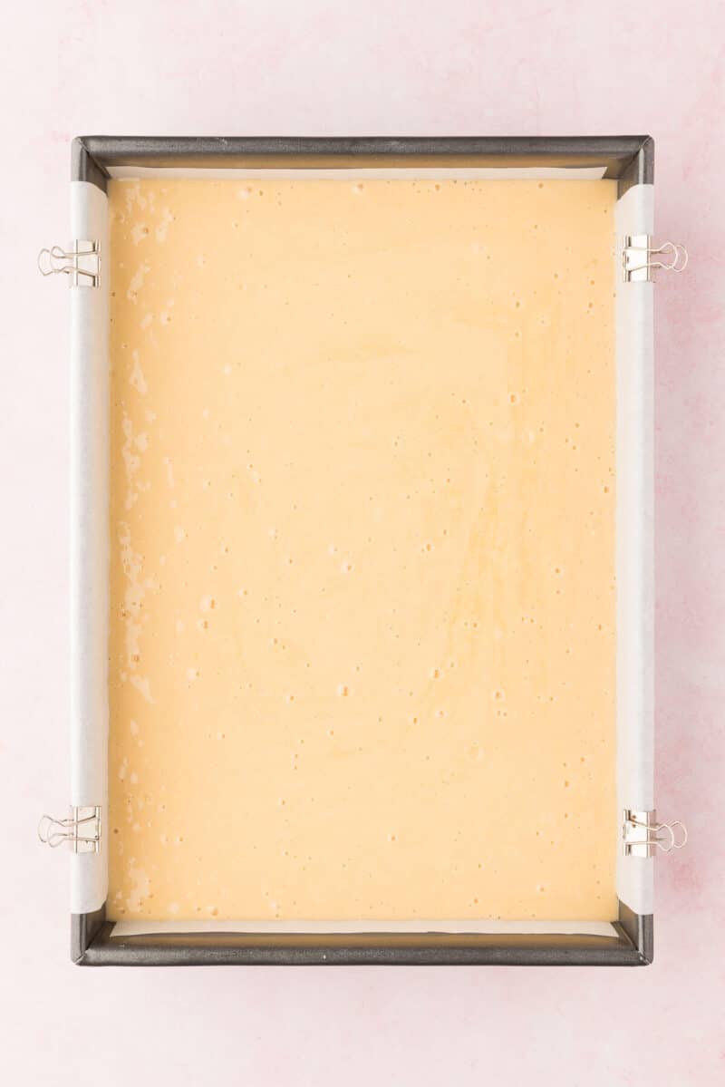 Unbaked cake batter in a rectangular metal baking pan on a pink surface.