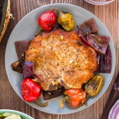 Pork chop served on a bed of cherry peppers on a wooden table.