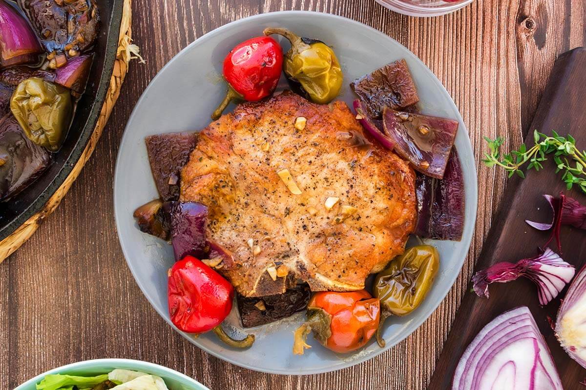Pork chop served on a bed of cherry peppers on a wooden table.