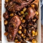 A dish of Julia Child's Coq au Vin with chicken, mushrooms, pearl onions, and herbs, served in a white rectangular dish.