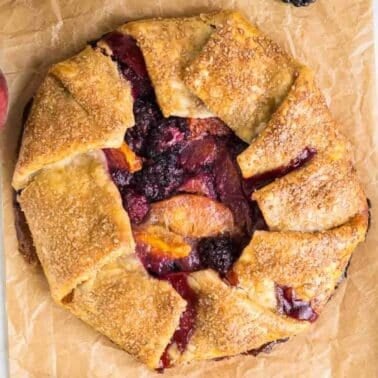 A rustic peach galette featuring a golden, flaky crust filled with a mix of baked berries and peach slices on parchment paper.