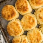 A baking tray holds eight golden-brown, freshly baked old-fashioned buttermilk biscuits on a marble surface.