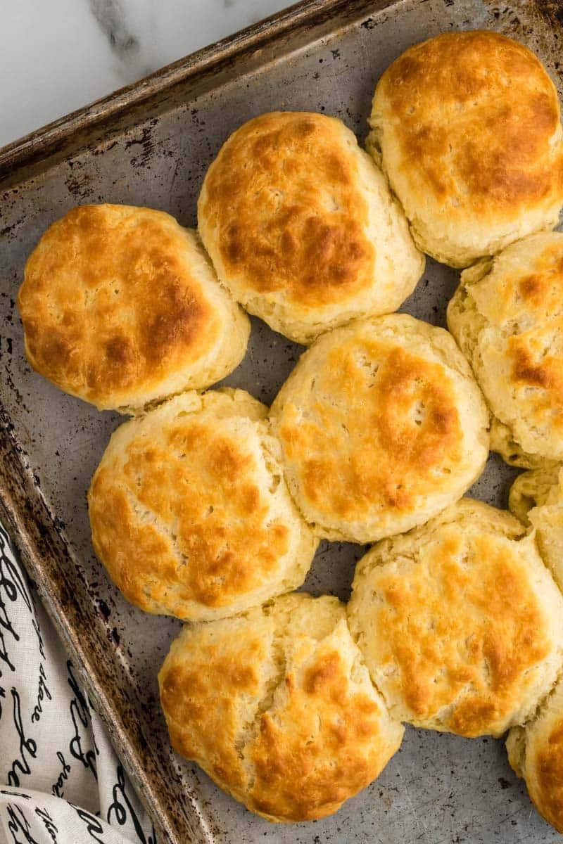 A baking tray holds eight golden-brown, freshly baked old-fashioned buttermilk biscuits on a marble surface.