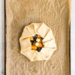 An unbaked rustic tart filled with fruit is placed on a sheet pan lined with brown parchment paper.