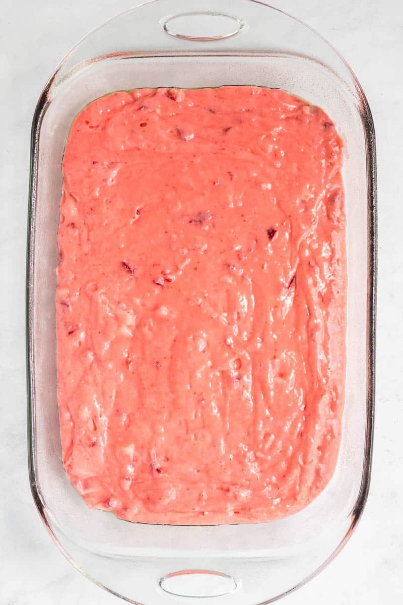 Glass baking dish filled with pink, strawberry-flavored batter, ready for baking.