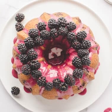 Bundt cake topped with pink icing and fresh blackberries, displayed on a white plate.