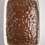 A white rectangular baking dish filled with a chocolate dessert with a textured surface. The edges of a white crust are visible along the sides. A blue cloth is partially seen in the lower left corner.