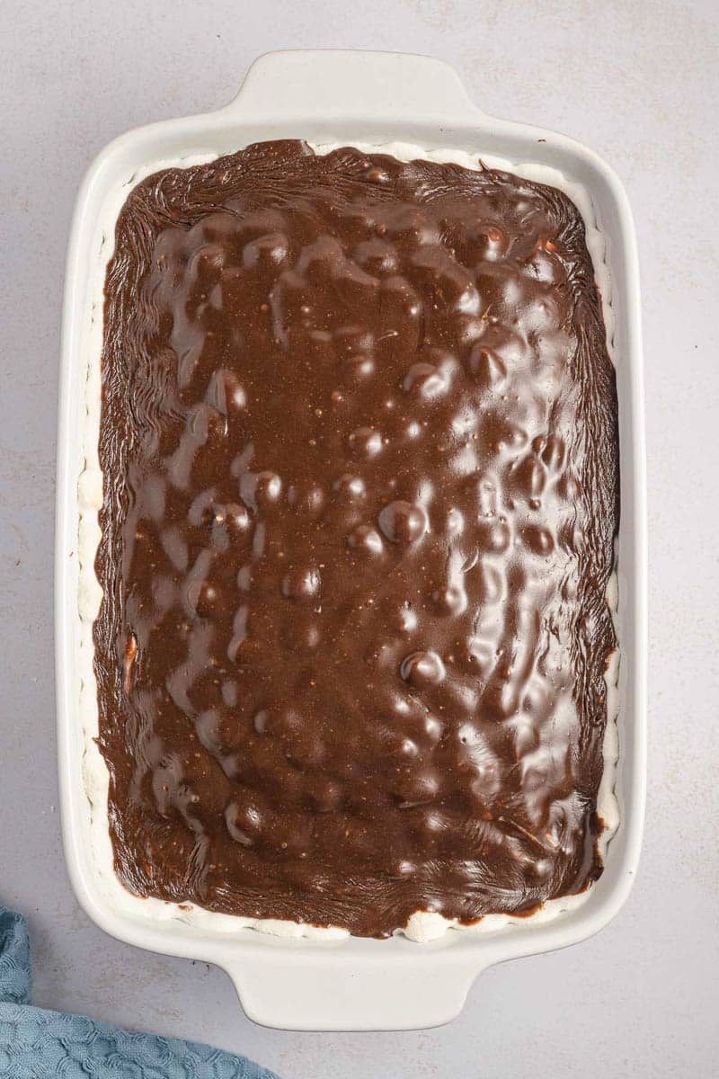A white rectangular baking dish filled with a chocolate dessert with a textured surface. The edges of a white crust are visible along the sides. A blue cloth is partially seen in the lower left corner.