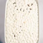 A rectangular baking dish filled with numerous small white marshmallows, surrounded by ingredients like butter and flour.