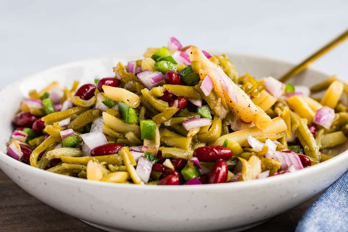 A bowl of three bean salad with green beans, yellow wax beans, kidney beans, chopped red onions, and diced green bell peppers.
