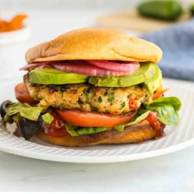 A turkey burger topped with avocado, tomato, lettuce, and pickled onions on a white plate.