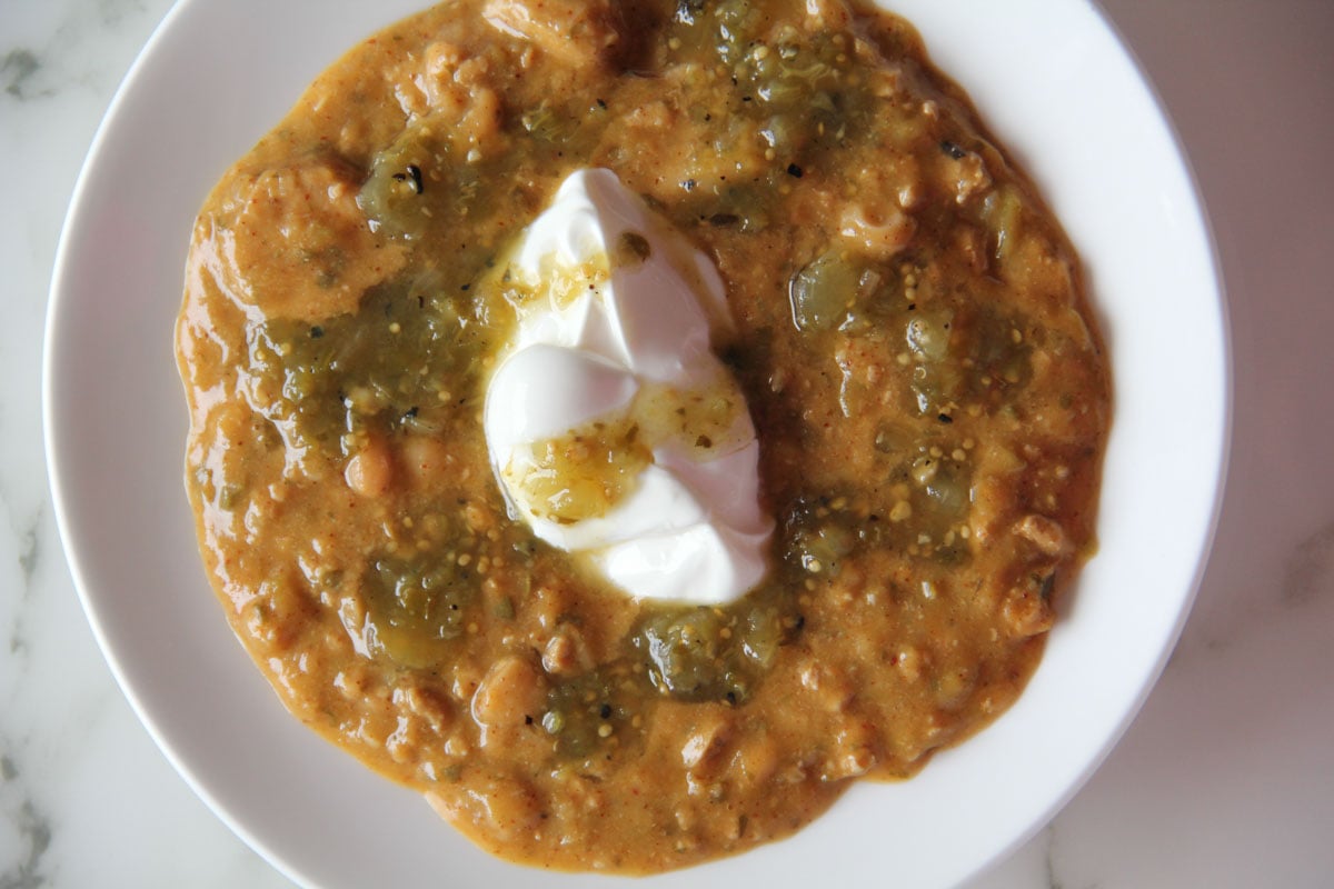 A bowl of chili topped with a dollop of sour cream on a white plate.