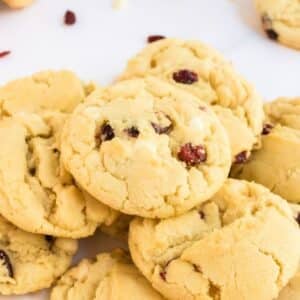 A pile of freshly baked cookies with visible bits of dried cranberries on a white surface.