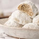 A plate filled with buttery pecan snowball cookies, with one cookie broken in half, revealing a crumbly interior.
