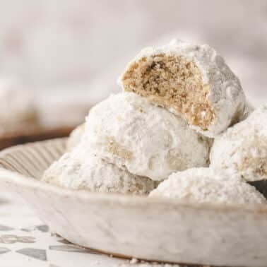 A plate of snowball cookies, with one broken to reveal a nutty interior.