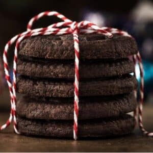 A stack of five chocolate cookies tied with red and white string on a wooden surface.