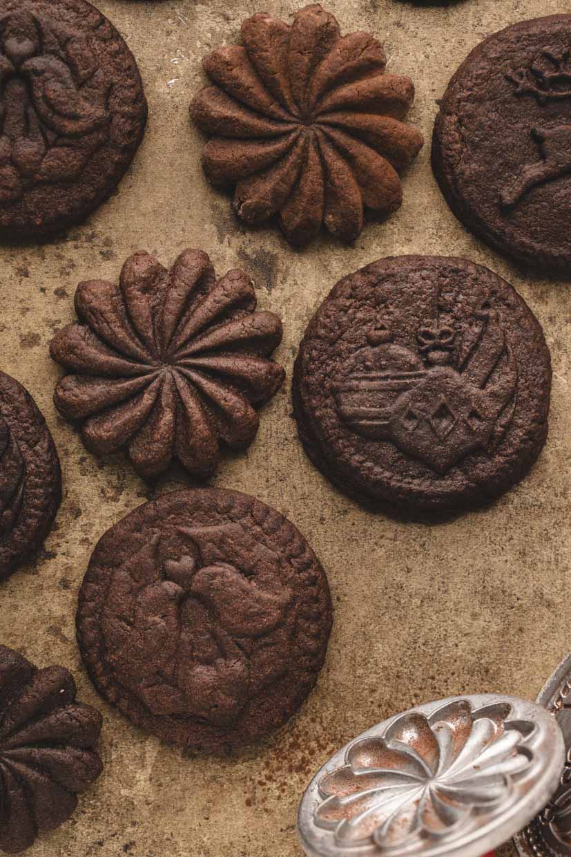 Various embossed chocolate cookies on a textured surface, with a metal mold nearby.