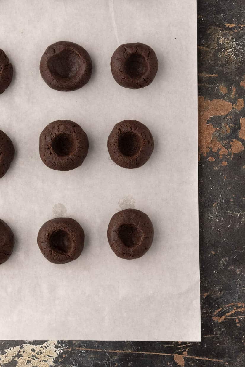 Nine round chocolate cookies with indentations arranged in a grid on parchment paper.