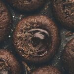 Close-up of chocolate thumbprint cookies with a glossy center and chocolate shavings on top.