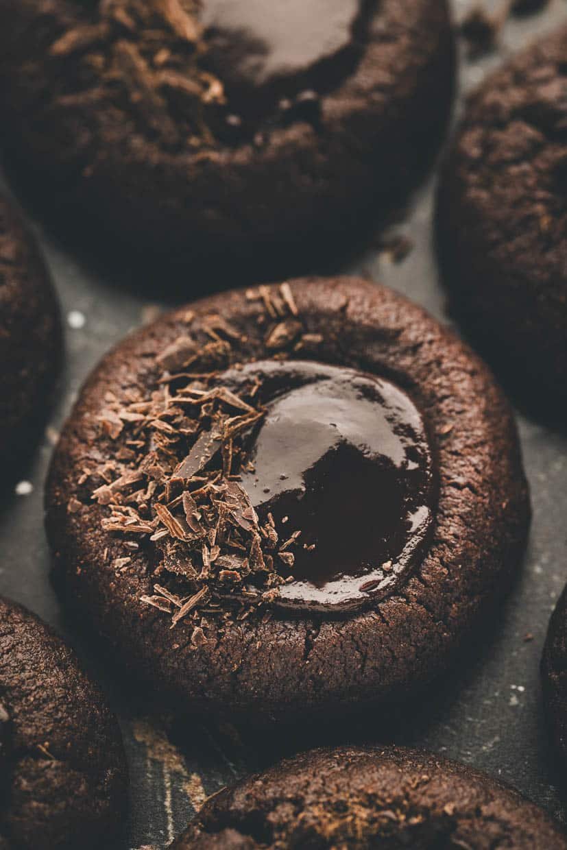 Close-up of a chocolate thumbprint cookie with a glossy center and chocolate shavings on top.