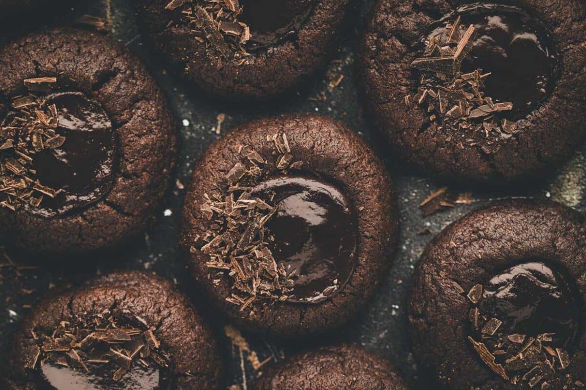 Close-up of several chocolate thumbprint cookies with melted centers and chocolate shavings on top.