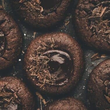 Close-up of several chocolate thumbprint cookies with melted centers and chocolate shavings on top.