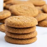 A stack of four sugar-coated cookies on a white surface, with more cookies blurred in the background.