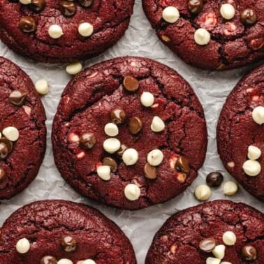 Red velvet cookies topped with white and dark chocolate chips on parchment paper.