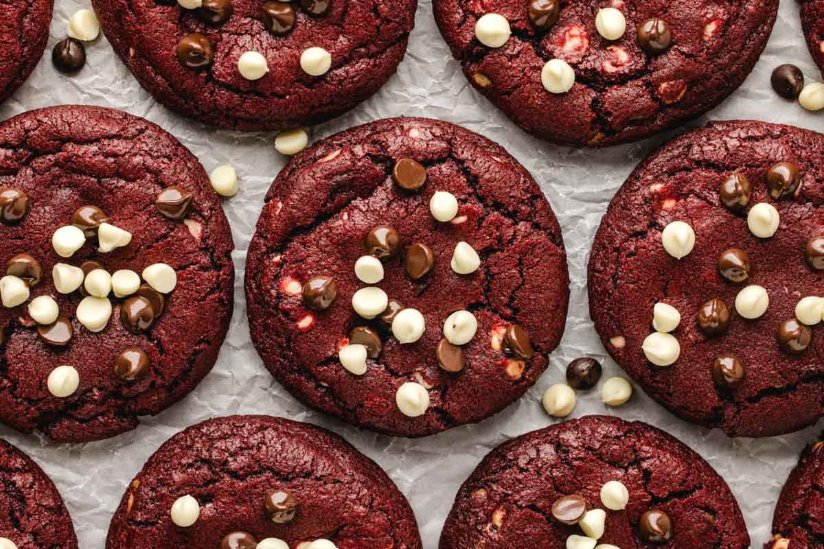 Red velvet cookies topped with white and dark chocolate chips on parchment paper.