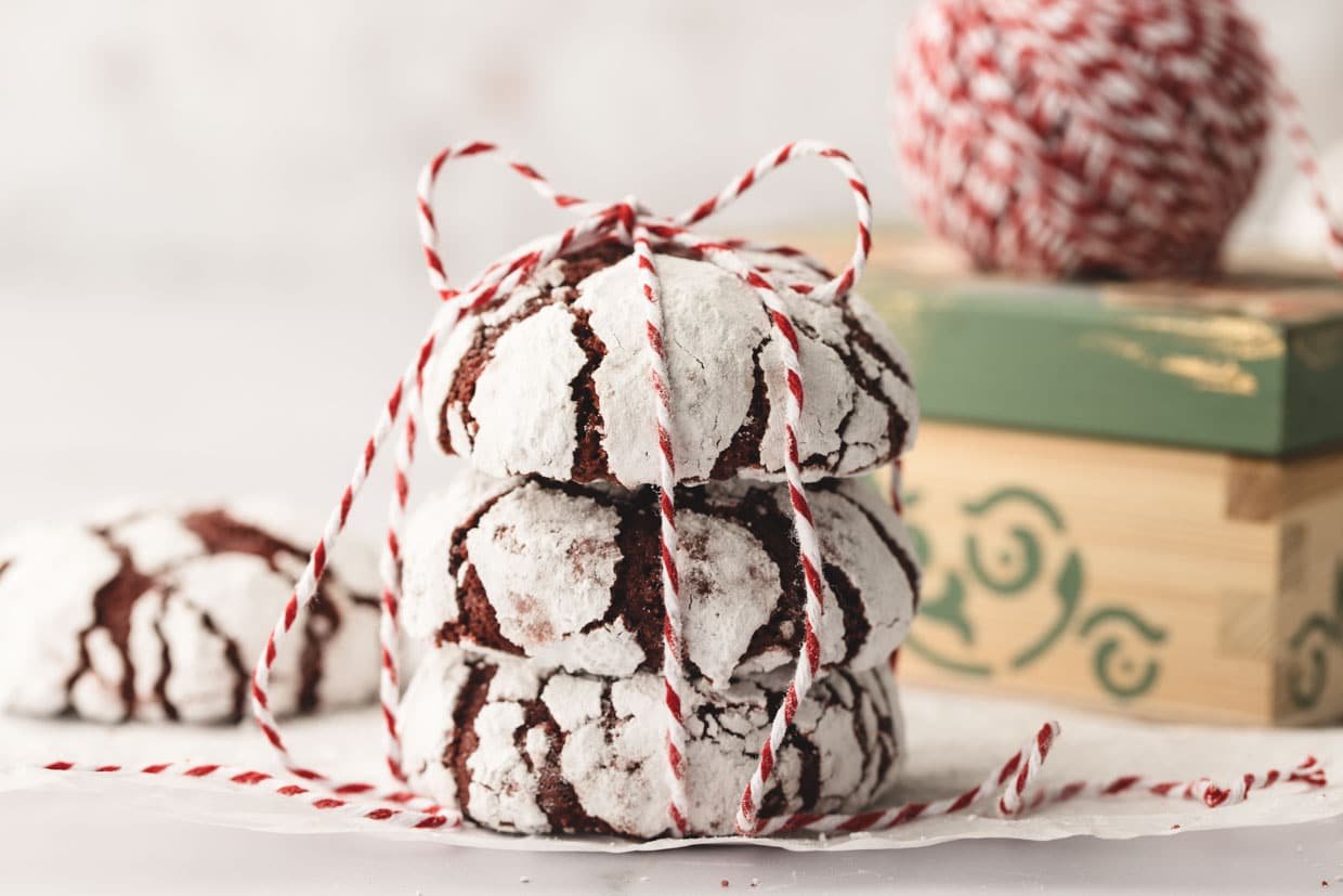 Three red velvet crinkle cookies tied with red and white string, placed on parchment paper. A ball of string and a green box are in the background.