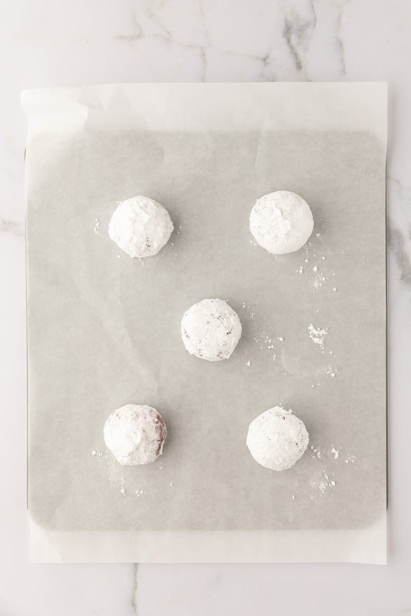 Five powdered sugar-covered balls arranged on parchment paper.