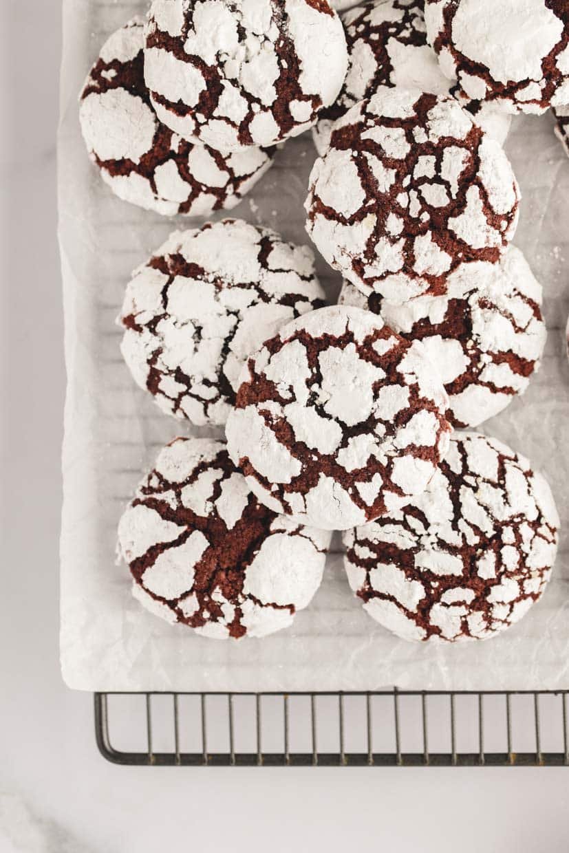 A stack of chocolate crinkle cookies dusted with powdered sugar on a parchment-lined cooling rack.