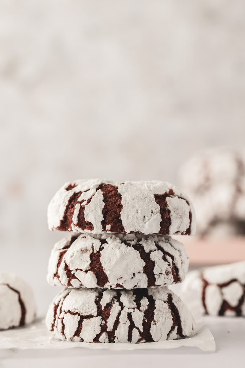 Three stacked chocolate crinkle cookies dusted with powdered sugar against a light background.