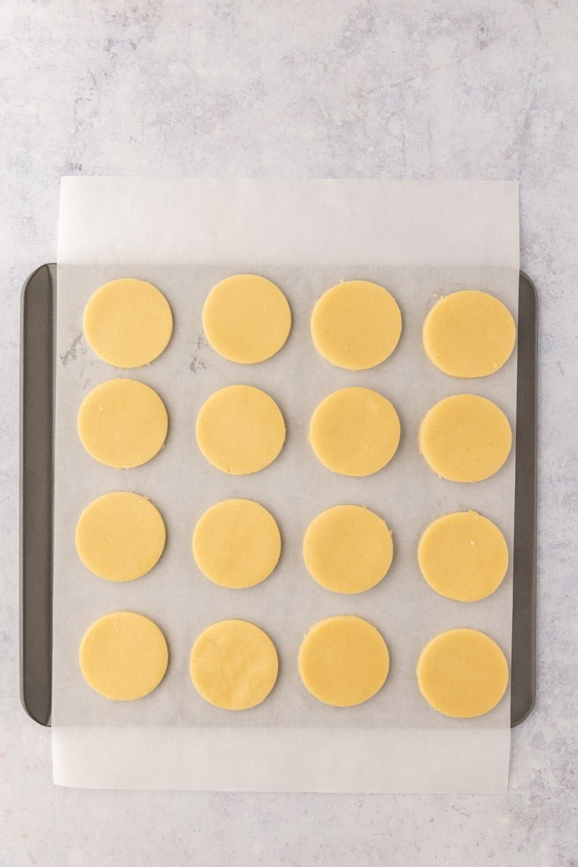 Round cookie dough discs evenly arranged on a parchment-lined baking tray, ready for baking.