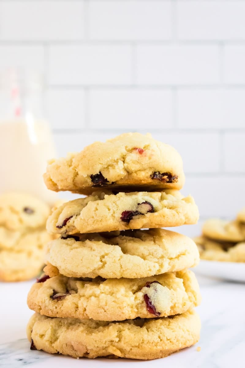 A stack of five buttery cookies with cranberries, set on a marble surface with a bottle of milk in the background.