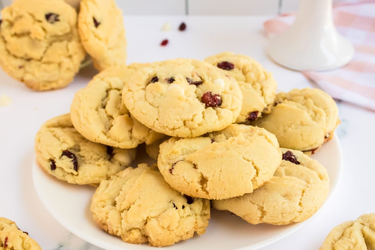 A plate of golden brown cookies with visible chocolate chips or raisins, stacked on a white surface.