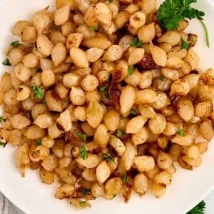 A plate of roasted pearl onions garnished with fresh herbs.