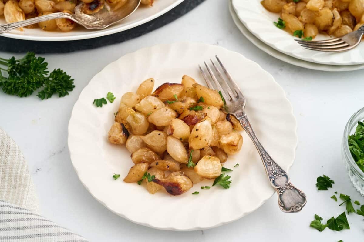 Plate of roasted pearl onions garnished with parsley, set on a white plate with a fork.