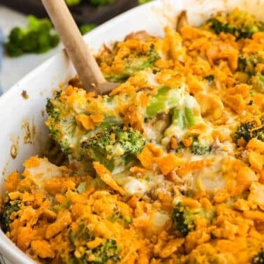 A baking dish filled with broccoli casserole topped with crispy, golden cheese and breadcrumbs, with a wooden spoon partially inserted.