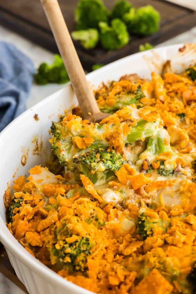 A baked broccoli and cheese casserole topped with crushed crackers in a white dish, with a wooden spoon.