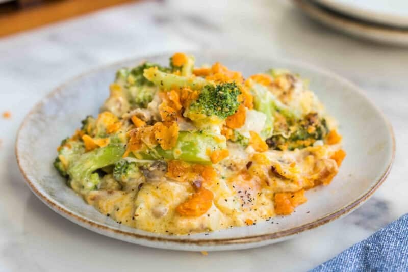 A baked broccoli casserole topped with crushed cheddar crackers, served in a white dish with a wooden spoon—one of the best fresh broccoli ideas for easy, comforting broccoli dishes.