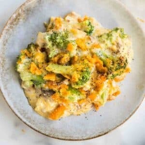 A plate of Southern broccoli casserole topped with melted cheese and black pepper, served on a beige dish.